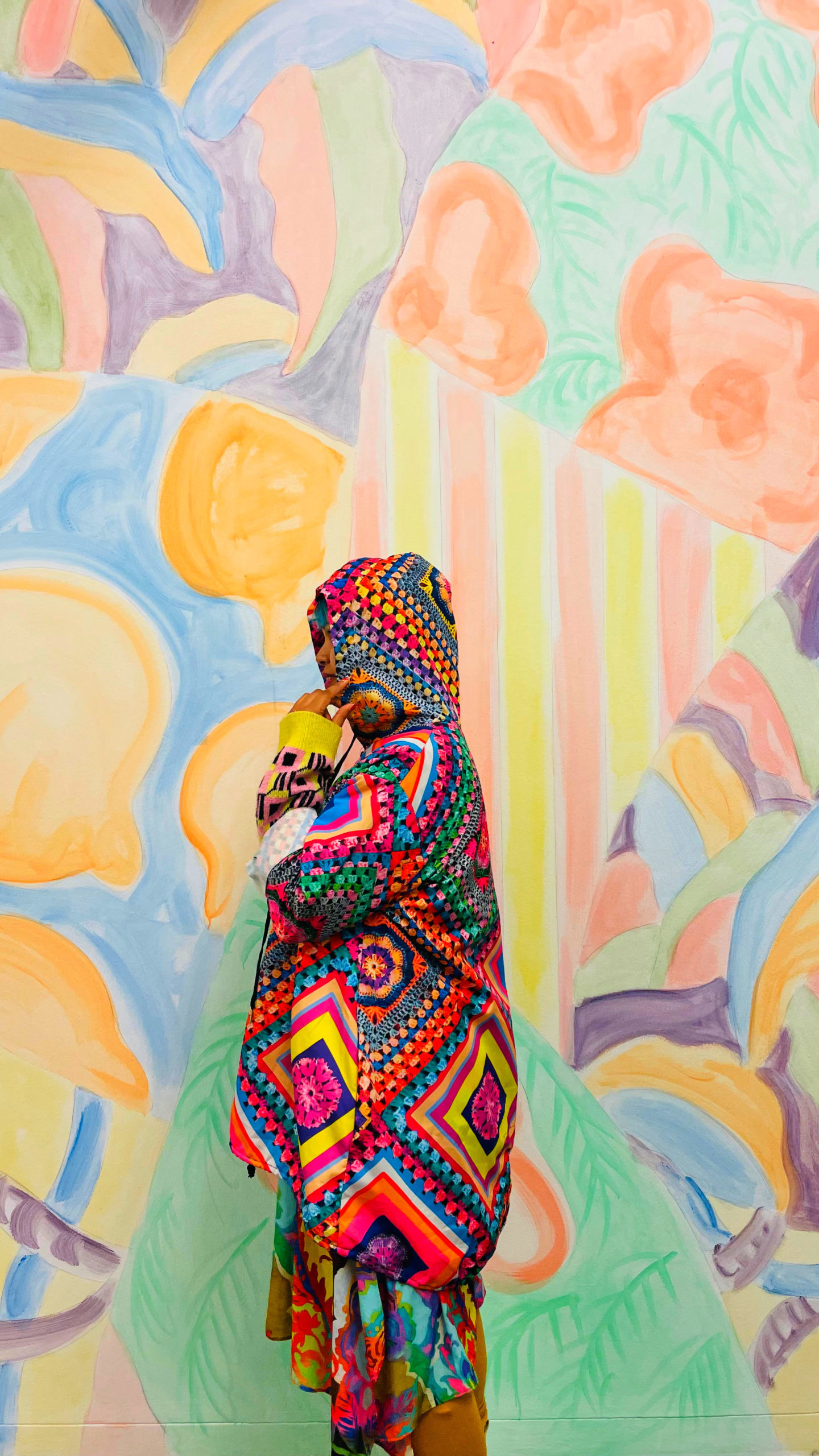 wall of colourful art with person standing profile in raincoat infront