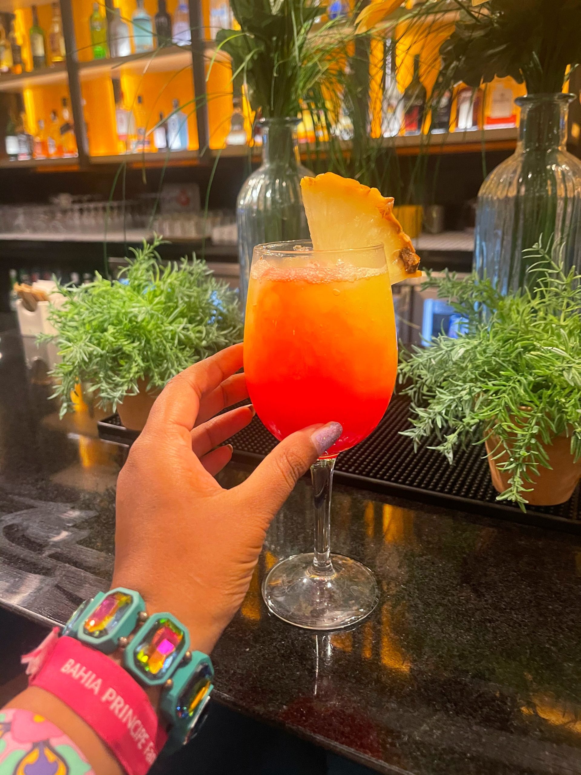 hand reaching for a orange coloured non alcoholic cocktail with pineapple chunk in it