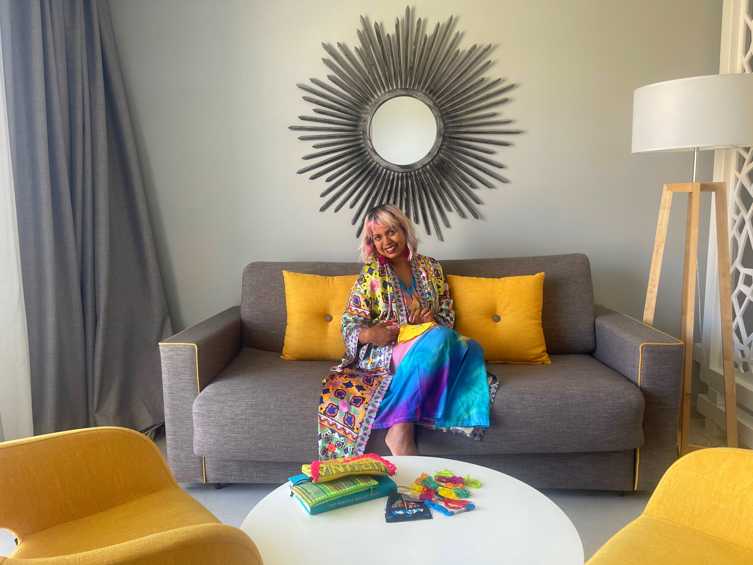 girl sat on sofa with yellow cushions on table in front is a pile f craft supplies