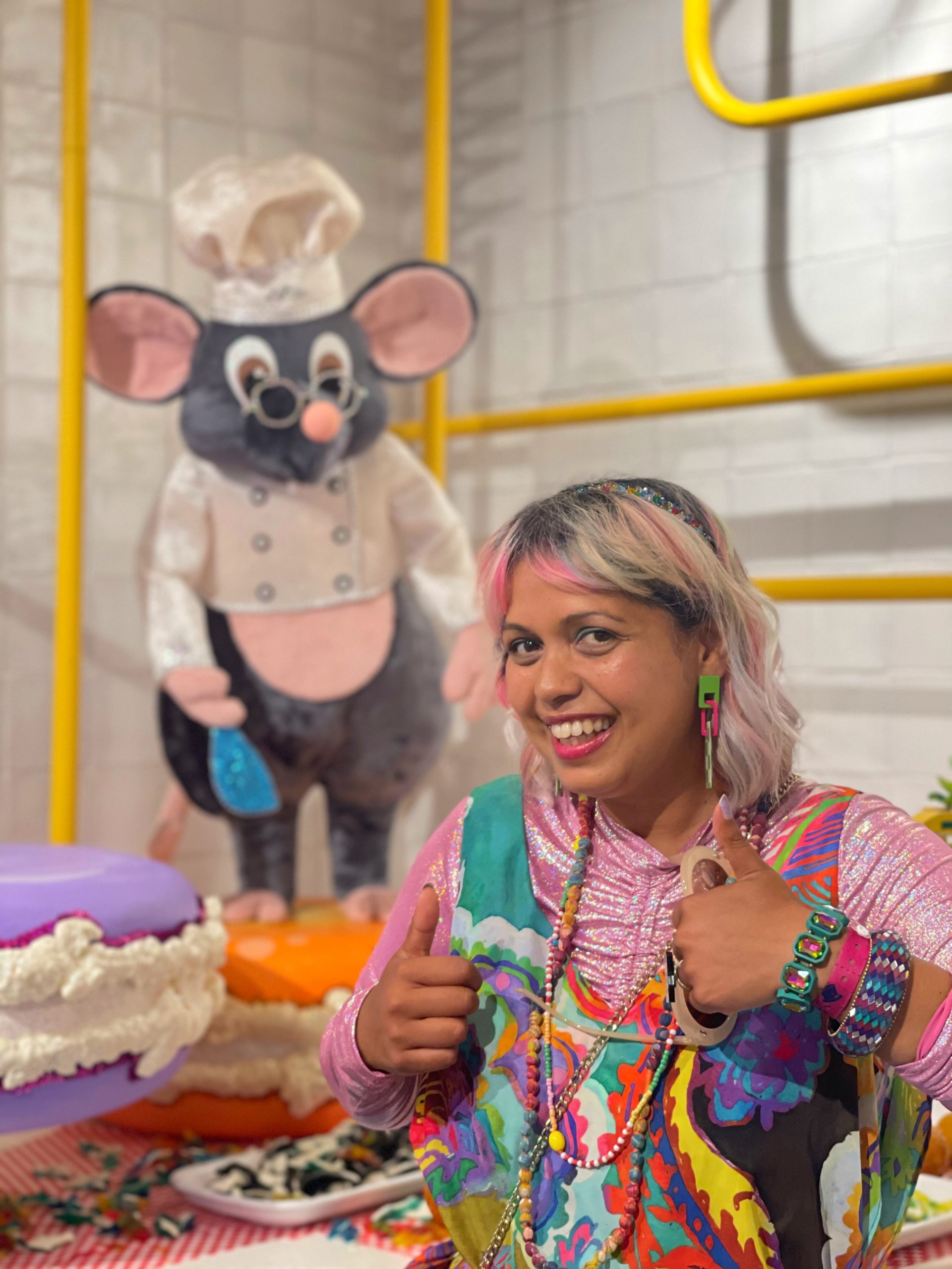 colourful hotel tenerife colourfully dressed girl with thumbs up and a giant toy of Ratatouille the rat dressed as a chef in background