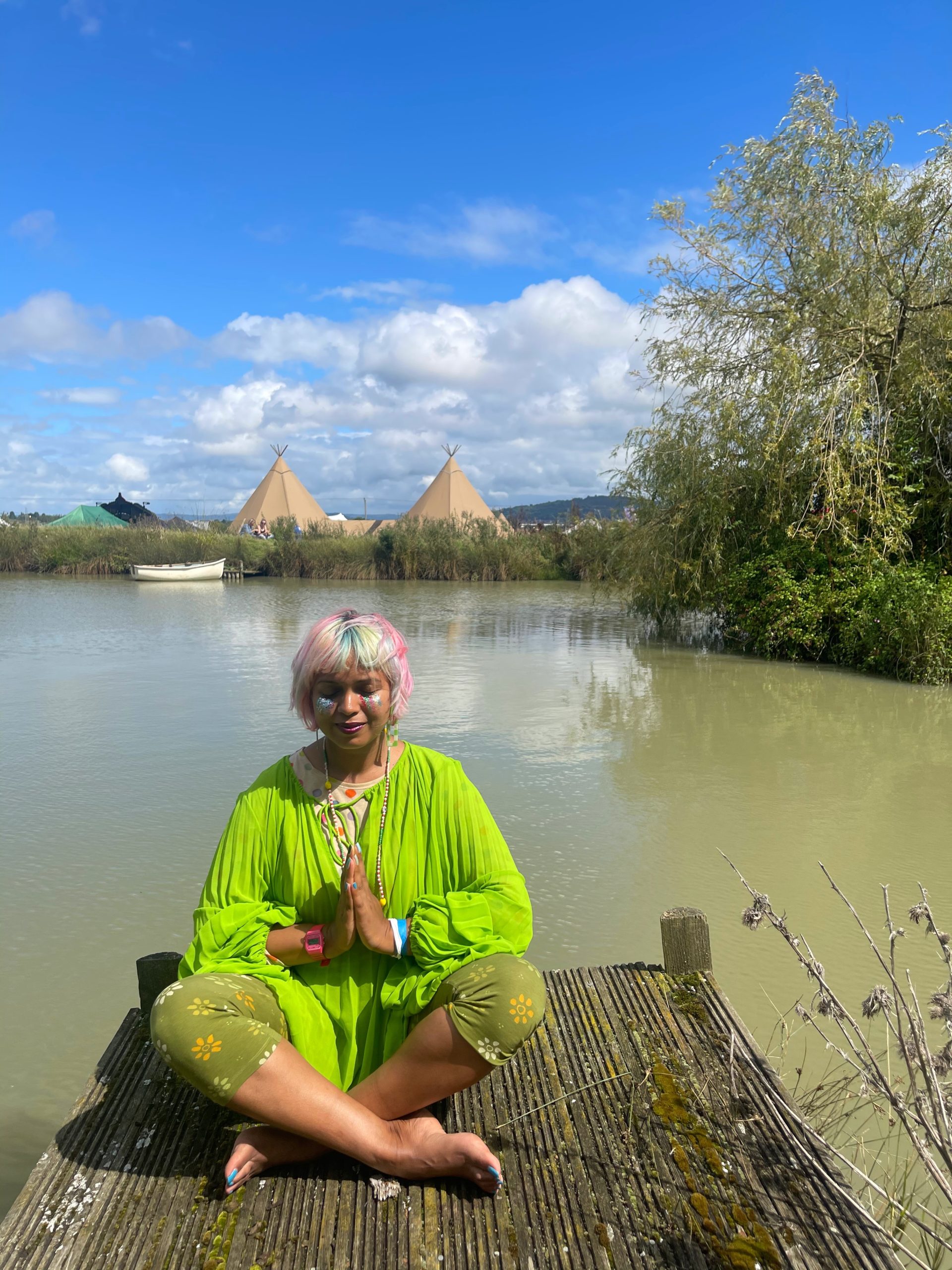Momtaz sat crossed legging hands in prayer position meditation in front of a lake