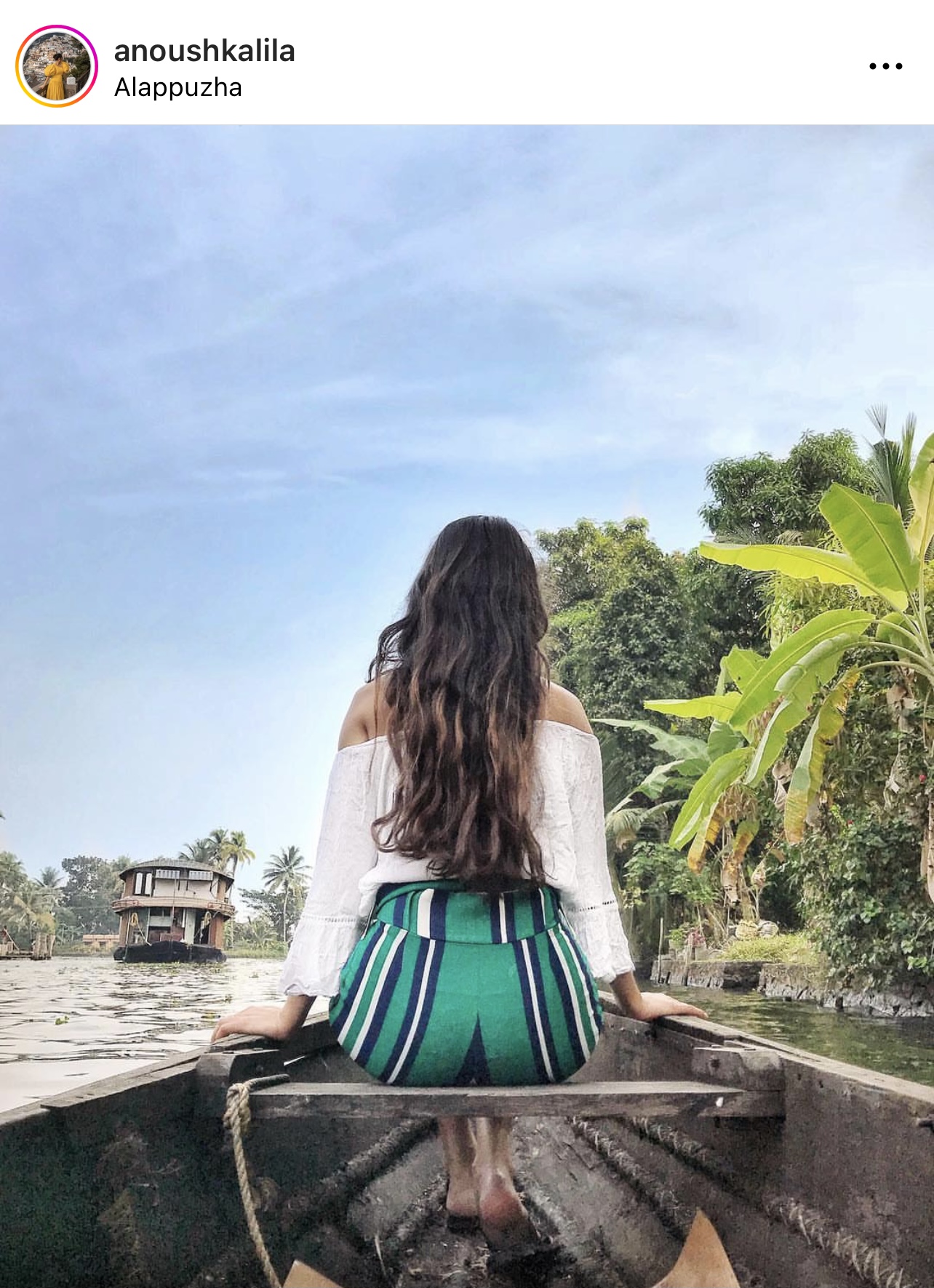 girl with long hair sitting on  a boat on the backwaters of kerala with her back towards us