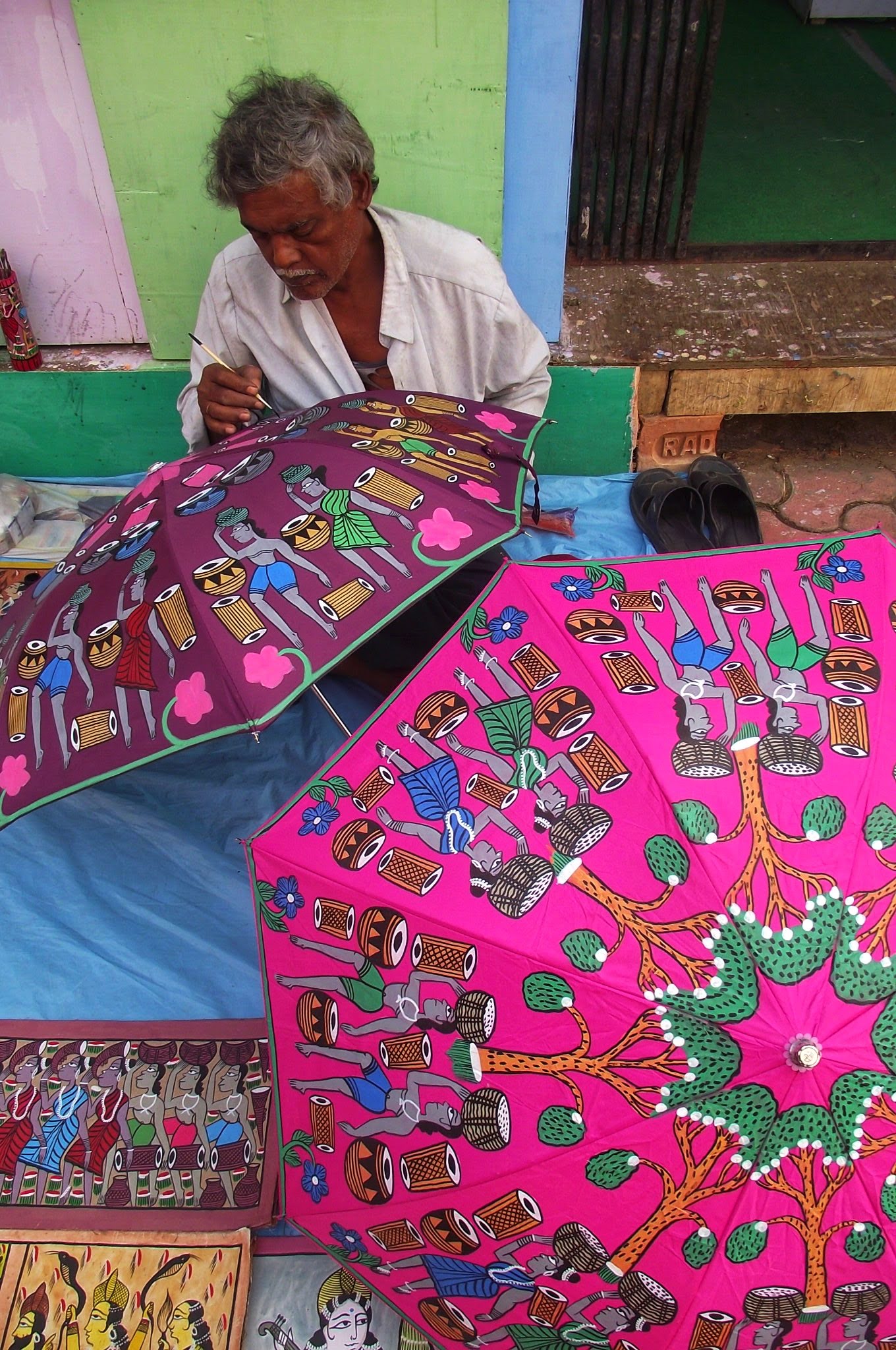 man on floor hand painting an umbrella in madhubani folk art style