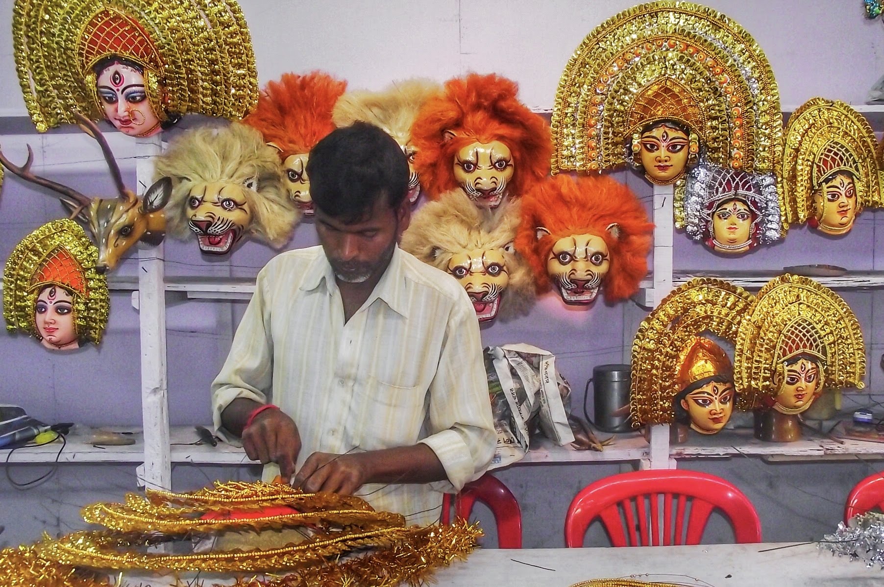 indian man making masks at  at a table behind him are his other creations
