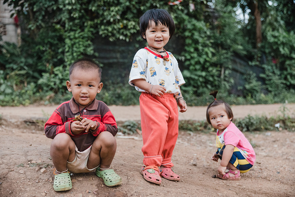 three very cute children crouching on the ground smiling to camera