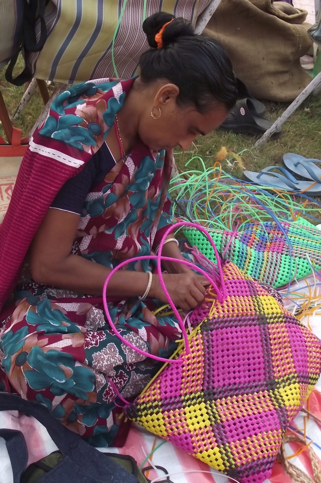 lady sat on grass concentrating on weaving a yellow and pink basket