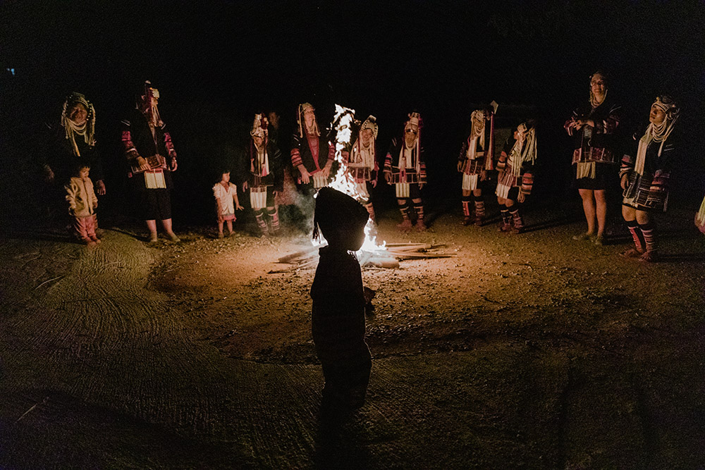 a night shot bonfire in middle, silouette of  a child in front and women behind in costume 