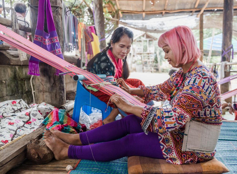 momtaz is sat on floor with a back strap loom tied around her waist weaving a ba