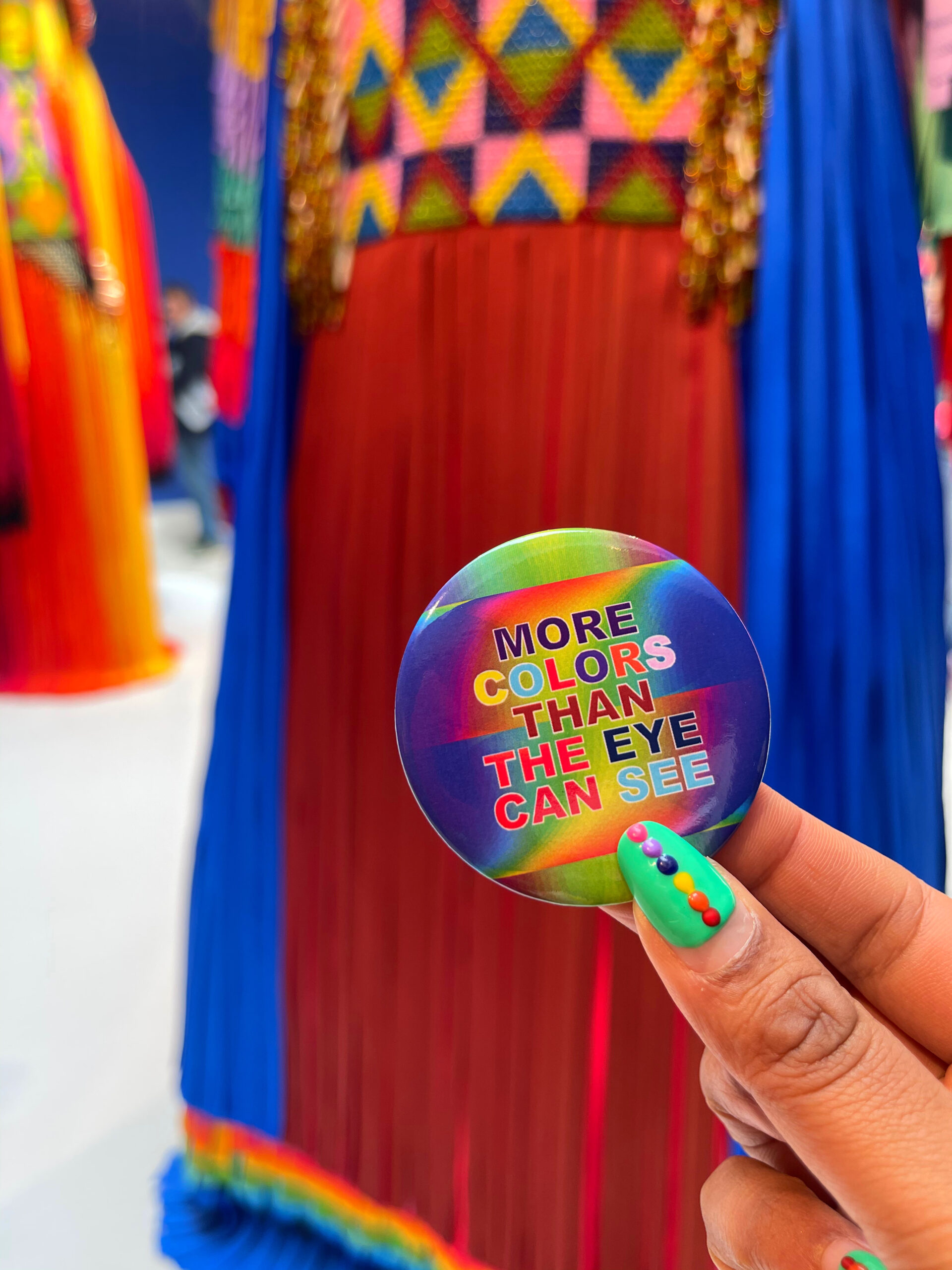 fingers holding a badge that says more colours than the eye can see