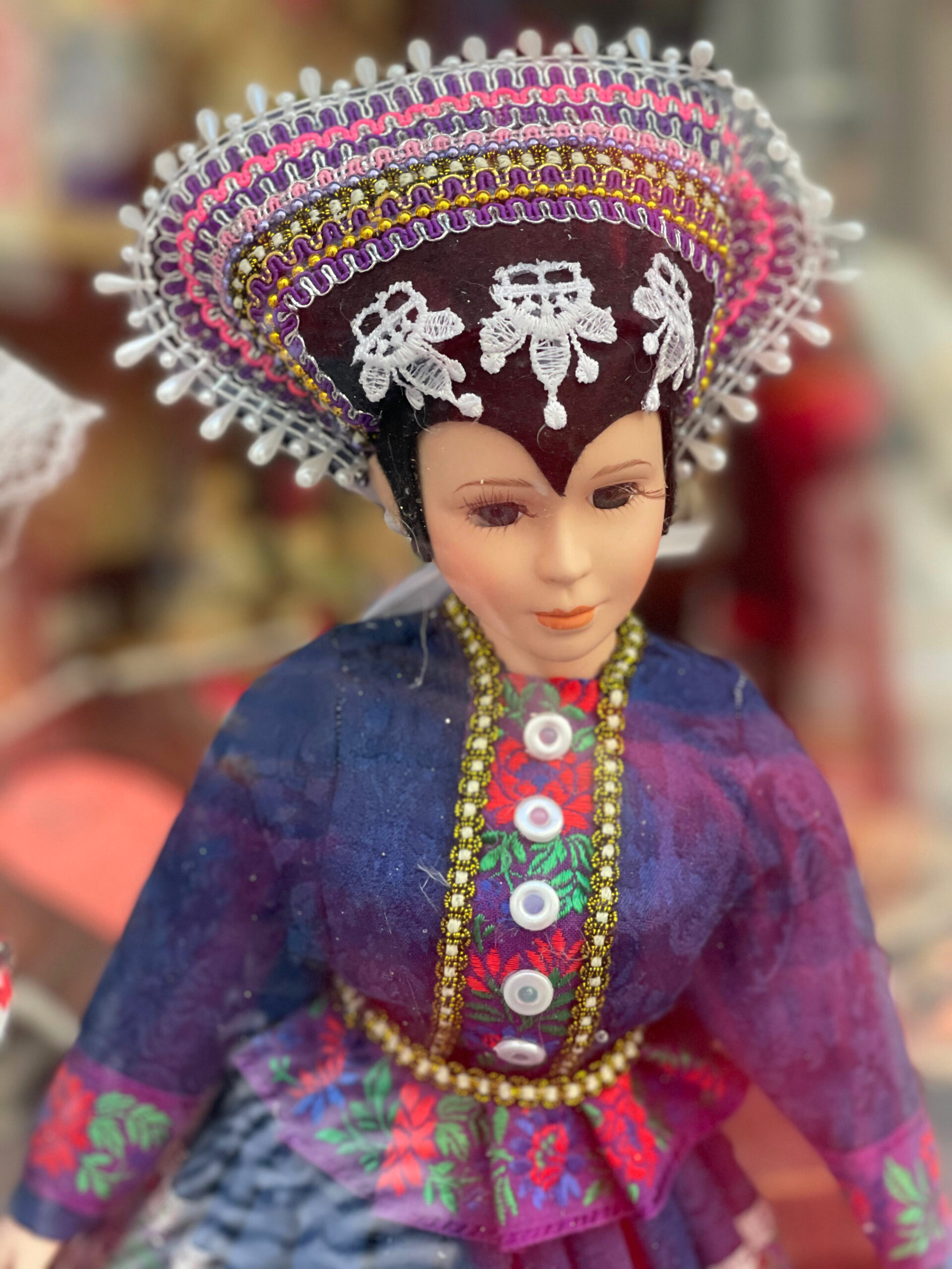 a doll dressed in a traditional blue blouse with embellished ribbon and elaborate hat