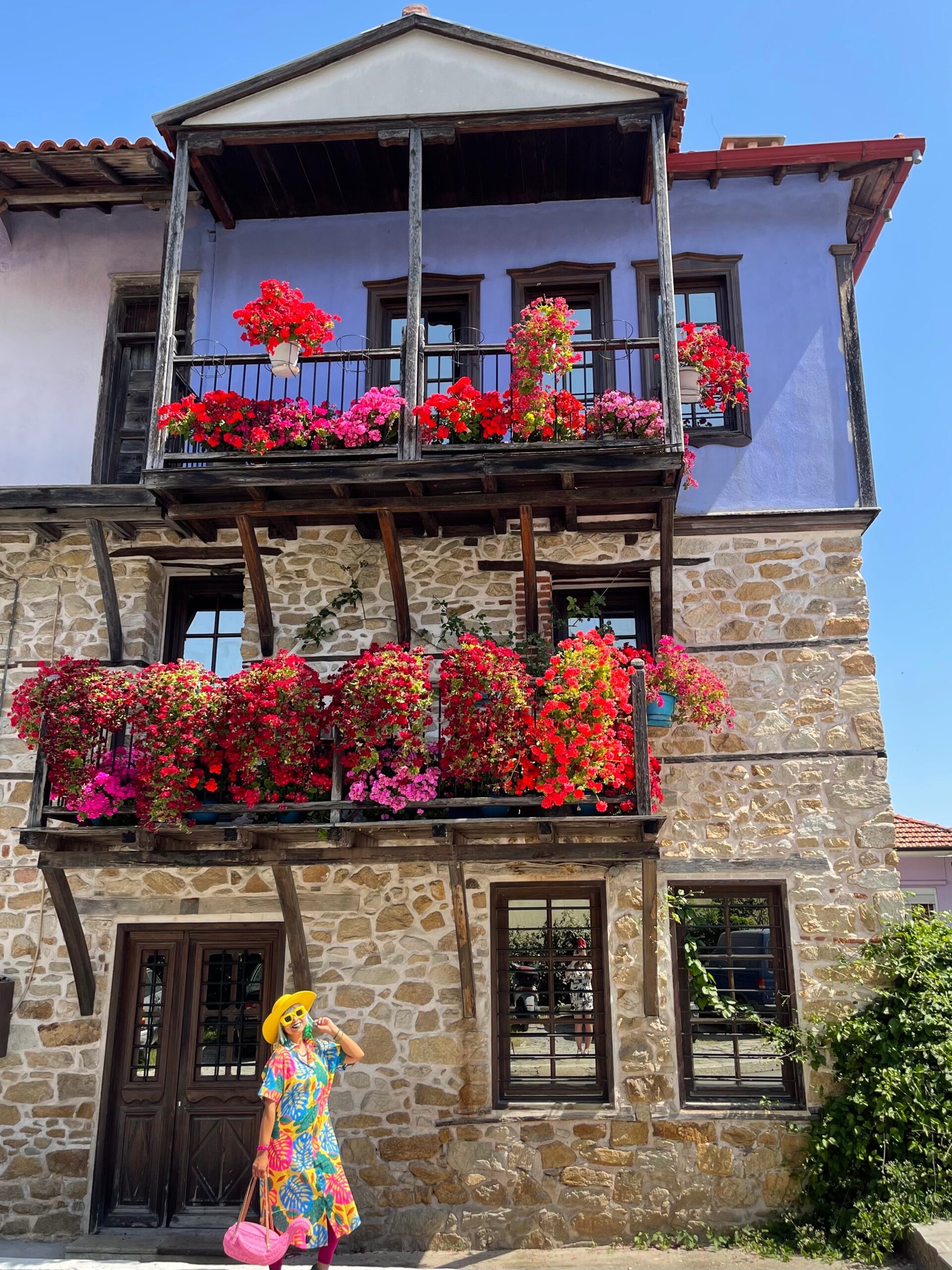 stone house with two balconies filled with flowers and a blue wall, halkidiki greece