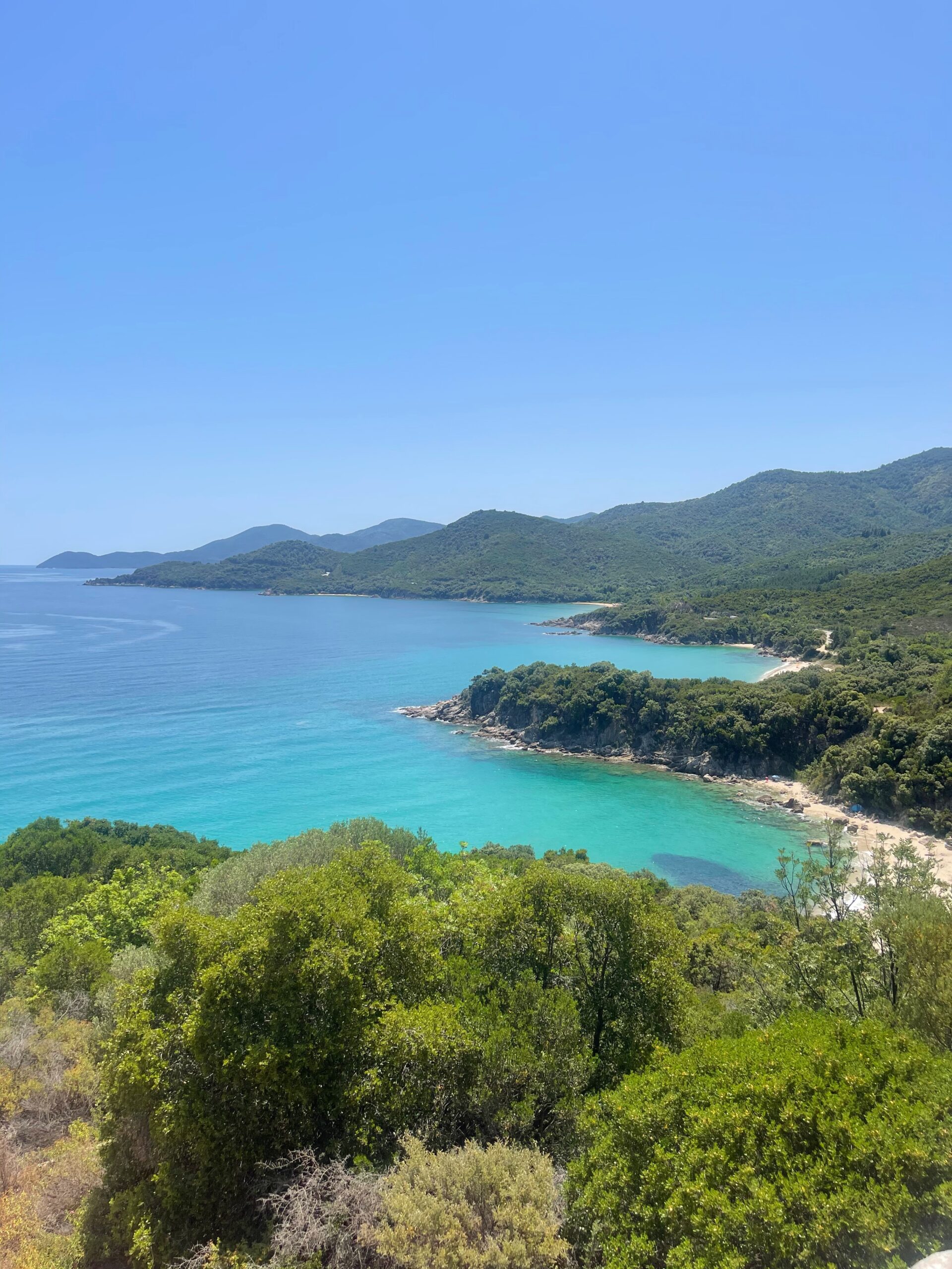 looking down as an aqua blue sea surrounded by trees, birthplace of aristotle, halkidiki