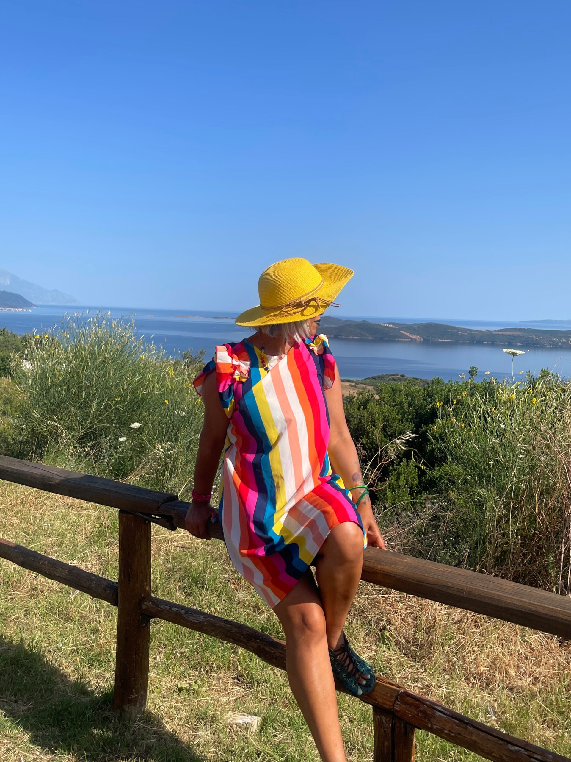 girl in stripey dress and sun hat leaning on a fence looking out to sea