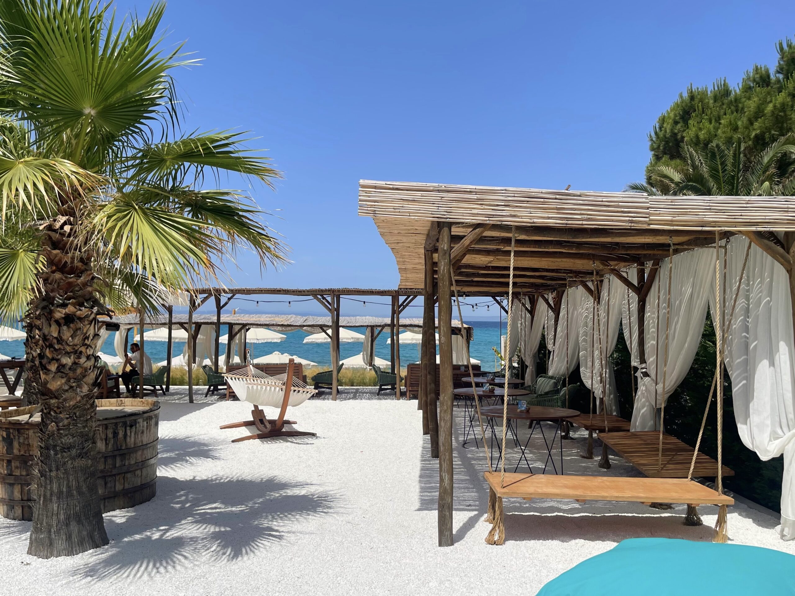 white sand beach with stylish seating , a hammock and palm trees, mare nosta beach club