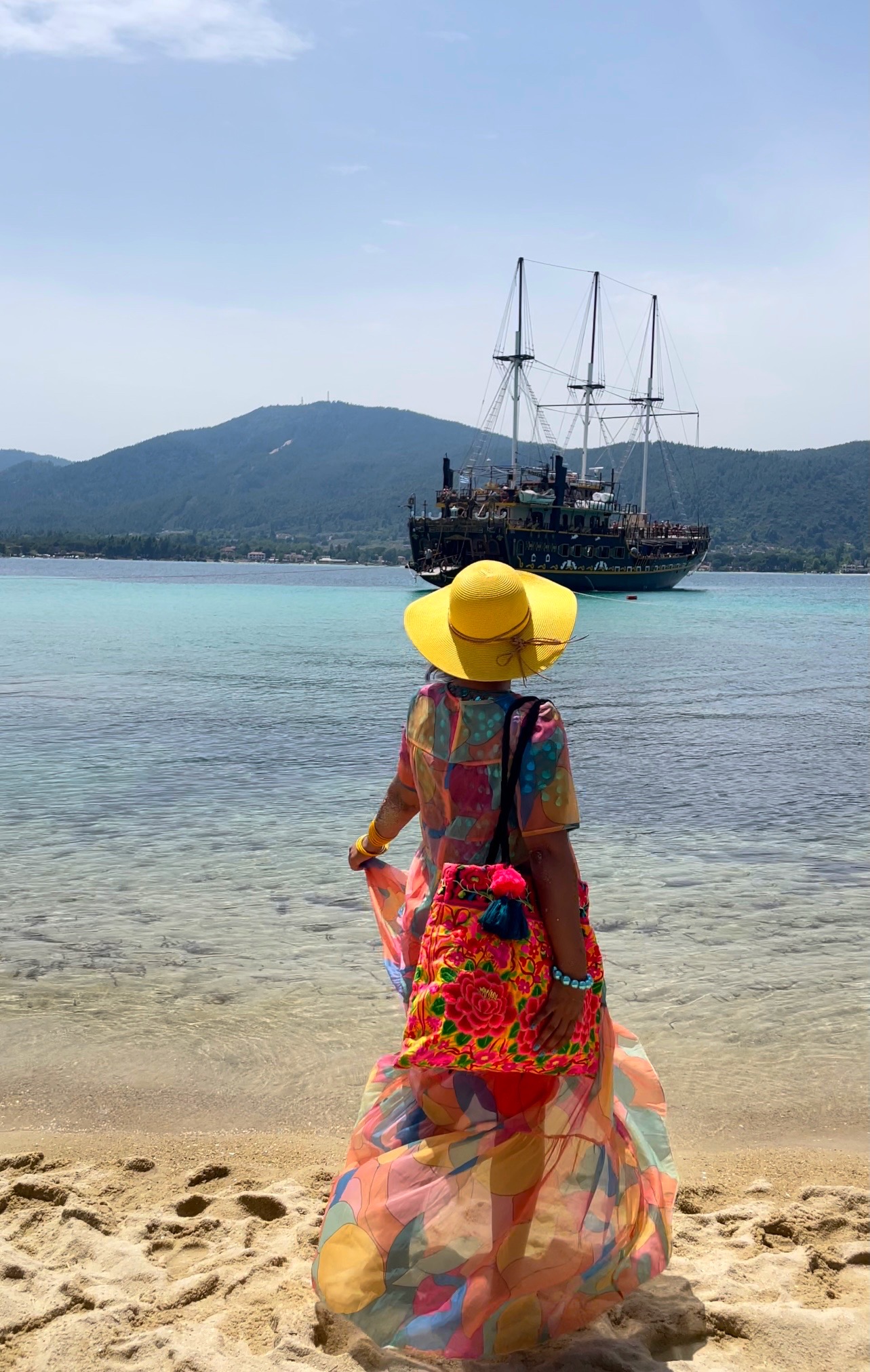 girl looking out to sea standing on sandy beach looking at a pirate ship, halkidiki