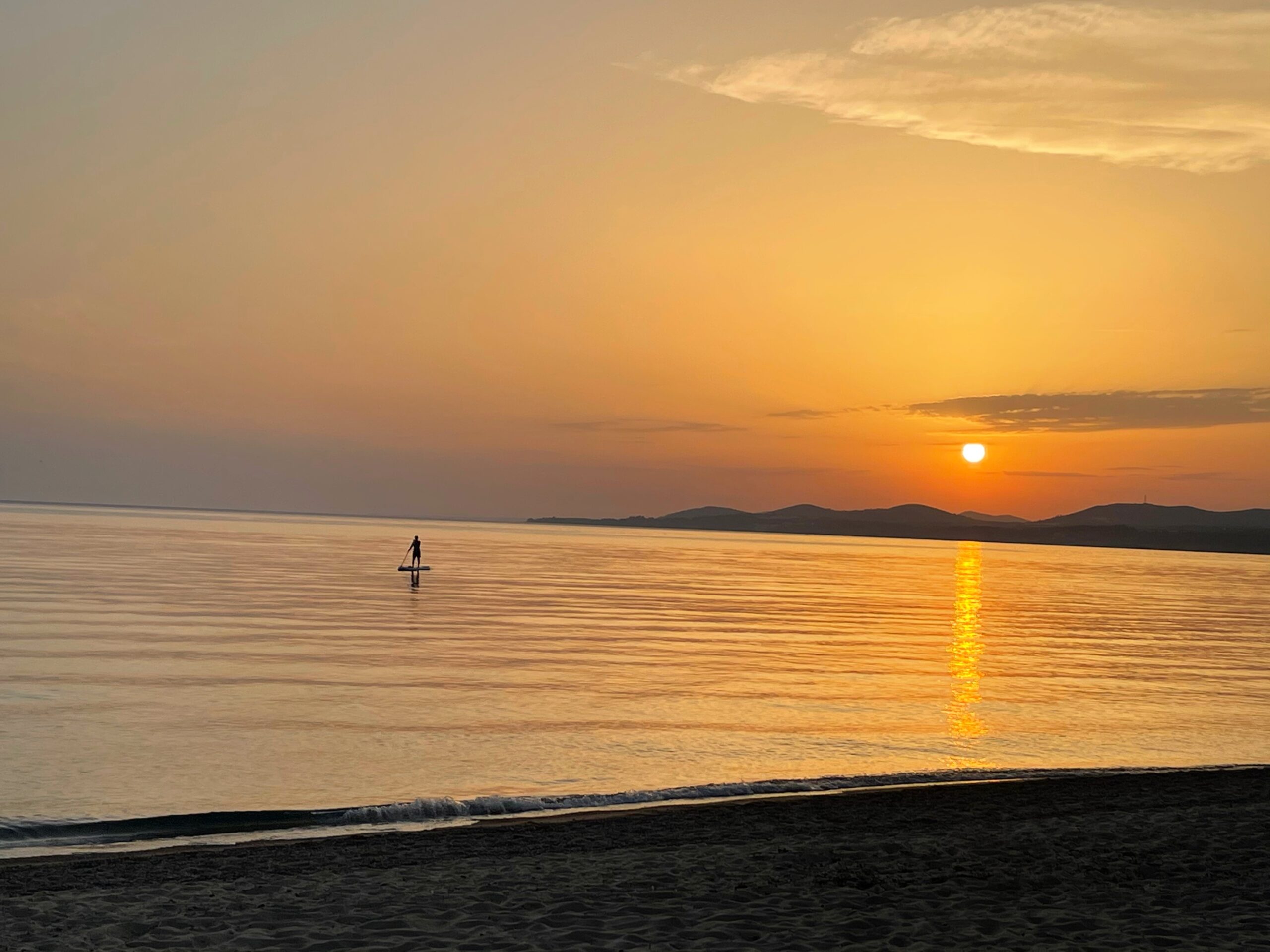 sunset on beach and silhoutte of a paddle boarder