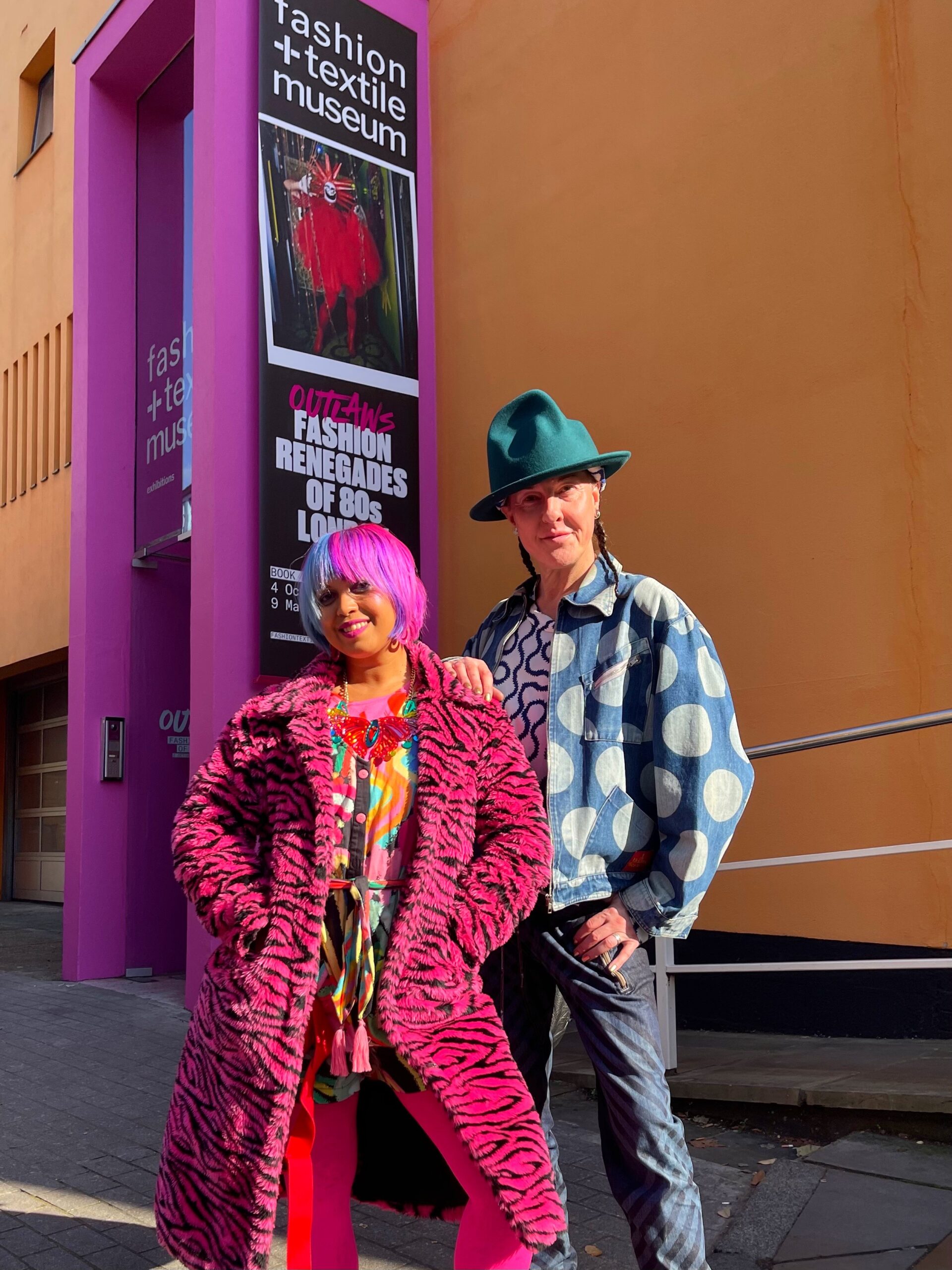 momtaz wearing a pink faux coat standing outside exhibition with maur